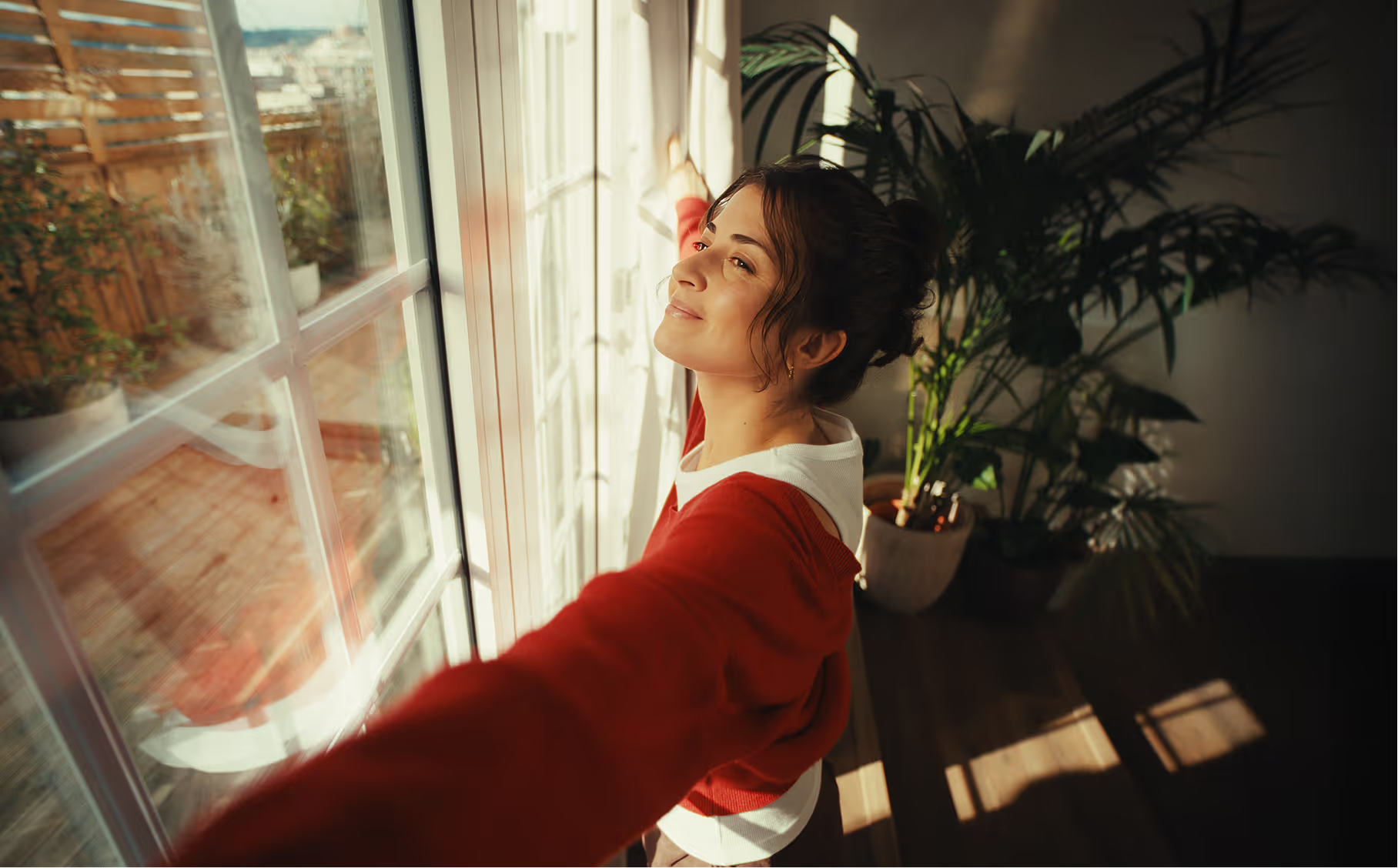 A woman opening a window onto morning sun in a bright, tidy flat