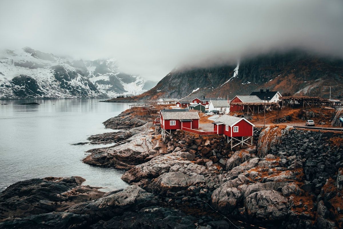 Holiday-let cabins on a rocky Norwegian shoreline, with a snow-covered fjord behind them